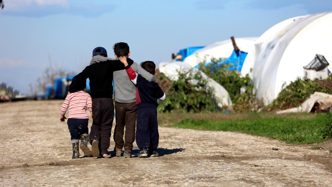 Vier kinderen lopen elkaar omhelzend, weg van de camera, over een zandweg