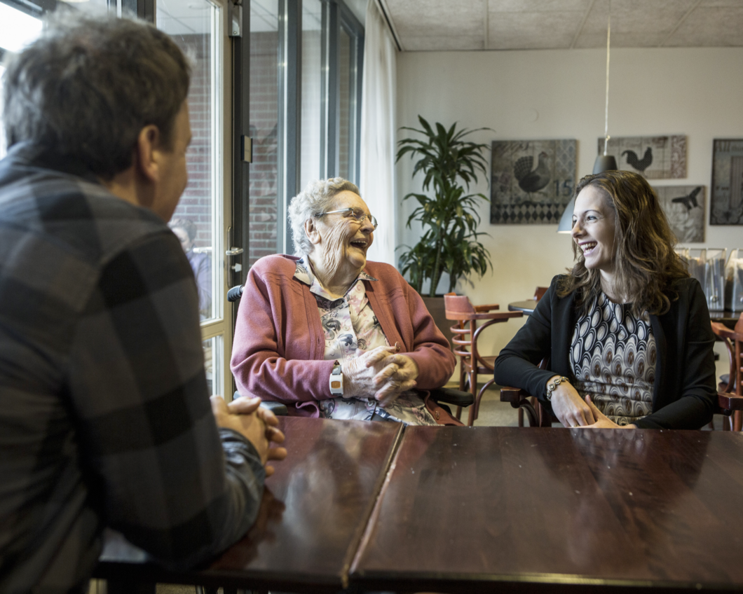 oudere vrouw lacht vrolijk tijdens een gesprek met haar mantelzorger